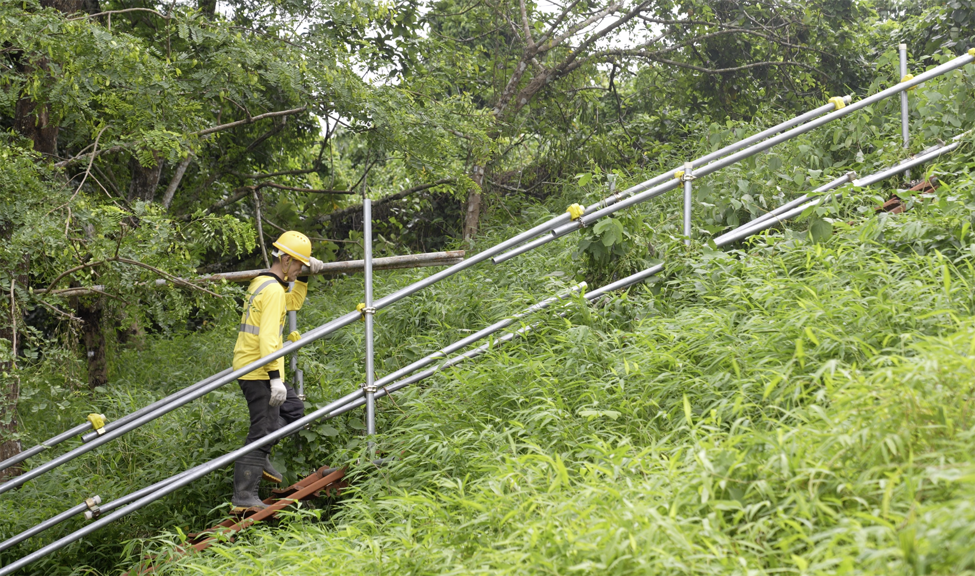 工人帶着十多公斤的物料「螞蟻搬家」地上落山坡，除了路徑陡峭，又要面對天雨、酷熱天氣的環境，搬運時一步一驚心，都為工地安全和職安健構成風險。
