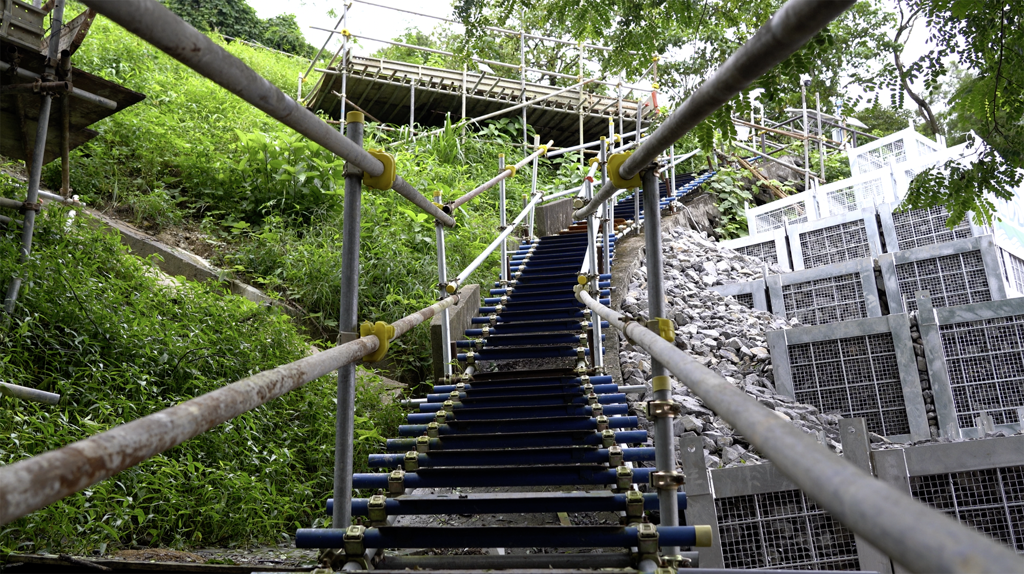 工人帶着十多公斤的物料「螞蟻搬家」地上落山坡,除了路徑陡峭,又要面對天雨、酷熱天氣的環境,搬運時一步一驚心,都為工地安全和職安健構成風險。 工人帶着十多公斤的物料「螞蟻搬家」地上落山坡,除了路徑陡峭,又要面對天雨、酷熱天氣的環境,搬運時一步一驚心,都為工地安全和職安健構成風險。